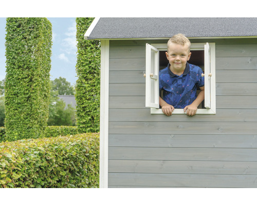 Kind schaut aus Fenster eines Holzspielhauses im Garten.