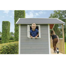 Kind spielt in grauem Holzspielhaus mit Rampe und Fenster