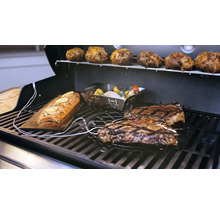 Grillszene mit Lachs auf Holzbrett, Steaks, Gemüse in einer Grillschale und Kartoffeln auf einem Grillrost