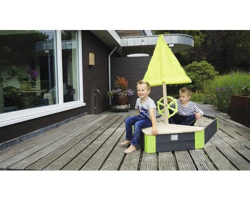 Sandkasten in Bootsform mit Segel und zwei spielenden Kindern im Garten.