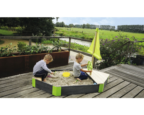 Sandkasten in Bootsform mit zwei spielenden Kindern im Garten.