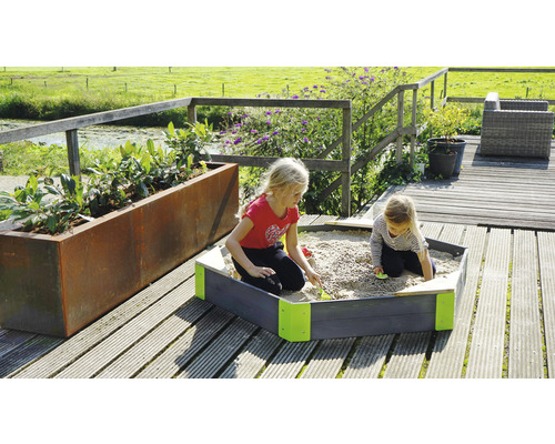 Zwei Kinder spielen im Sandkasten auf einer Holzterrasse neben einem Pflanzkasten.