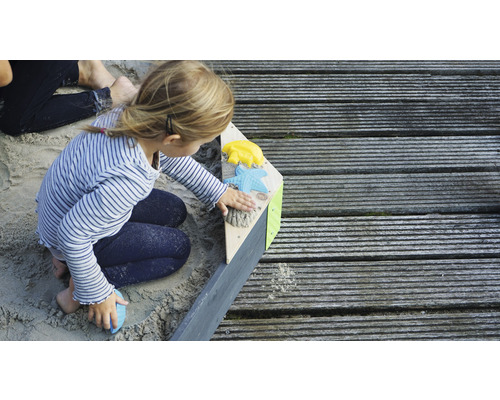 Mädchen spielt im Sandkasten mit Sandspielzeug auf Holzterrasse
