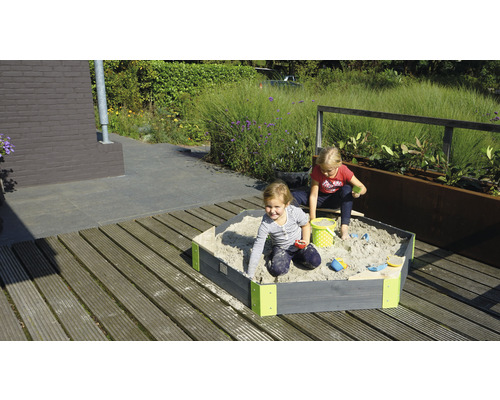 Zwei Kinder spielen in einem Sandkasten aus Holz im Garten.