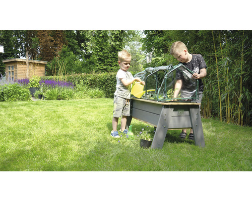 Zwei Kinder gießen und bepflanzen ein Hochbeet mit Frühbeetaufsatz im Garten.