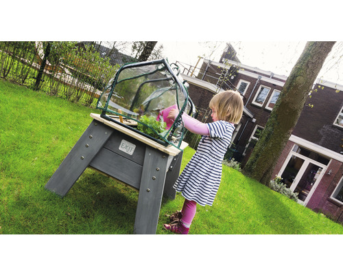 Kind gießt Pflanzen im Hochbeet mit Gewächshausaufsatz im Garten