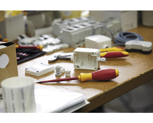 Aufnahme mit einer Auswahl an Elektrikerwerkzeugen und Installationsmaterialien auf einer Arbeitsfläche.