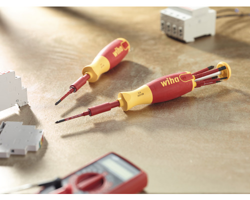 Wiha Logo, zwei Schraubendreher, Messgerät und elektrische Bauteile auf einer Arbeitsfläche.