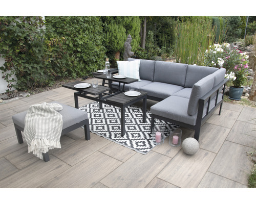 Gartenszene mit grauer Lounge-Eckgarnitur, Beistelltischen, Hocker und gemustertem Teppich auf einer Terrasse.