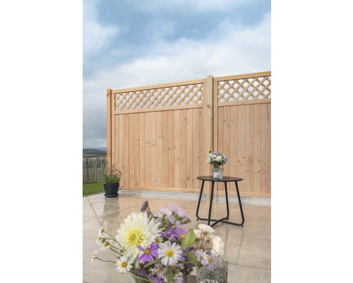 Gartenszene mit Holzzaun, kleinem Tisch und Blumenarrangements.
