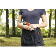 Eine Frau hält eine Handsäge vor einer Gartenschürze