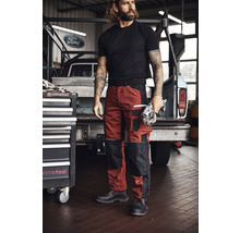 Mann mit Arbeitshose, T-Shirt und Sicherheitsschuhen vor Werkstattwagen und Pickup