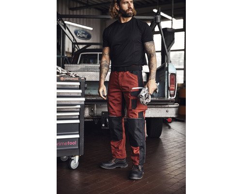 Mann mit Arbeitshose, T-Shirt und Sicherheitsschuhen vor Werkstattwagen und Pickup