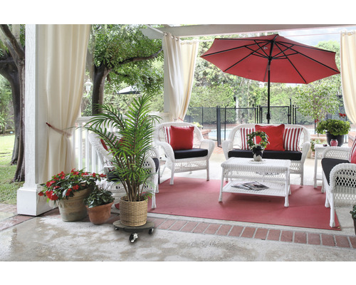 Terrasse mit weißen Rattanmöbeln, rotem Sonnenschirm und Topfpflanzen