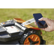 Ein Mann bedient einen Mähroboter mit einem Smartphone.