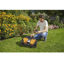 Mann bedient einen Mähroboter mit einem Smartphone im Garten.