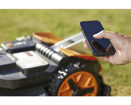 Ein Rasenmähroboter wird mit einem Smartphone gesteuert.