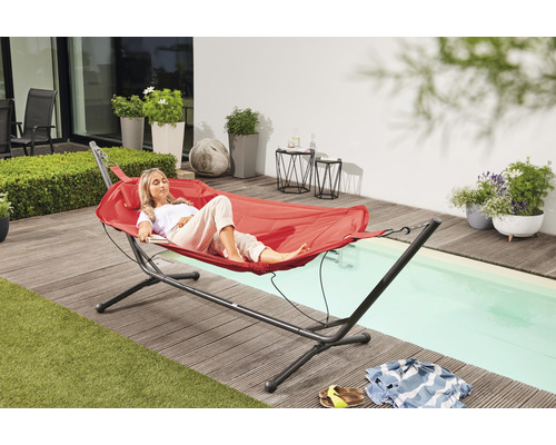 Frau entspannt auf einer roten Hängematte mit Gestell im Garten.