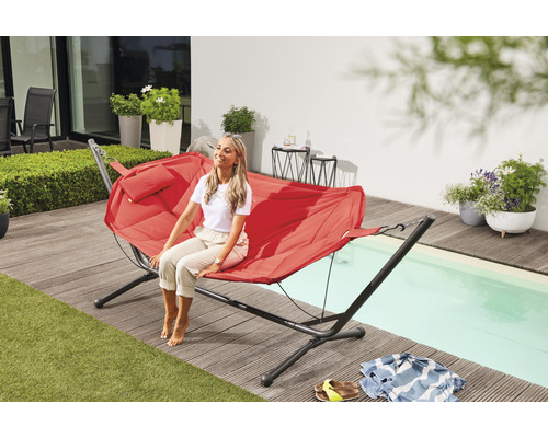 Frau entspannt sich auf einer roten Hängematte im Garten neben dem Pool