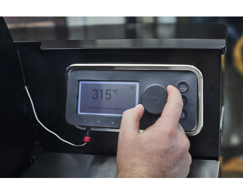 Nahaufnahme des Bedienfelds eines Grills mit Temperaturanzeige und Hand, die einen Drehknopf bedient