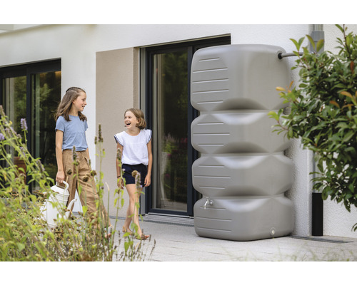 Regenwassertank mit Wasserhahn vor einem Haus, neben zwei Mädchen