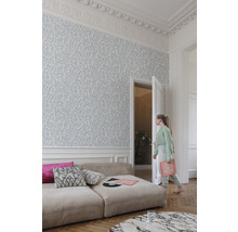 Heller Raum mit floral gemusterter Tapete, Sofa und einer jungen Frau, die durch eine offene Tür geht