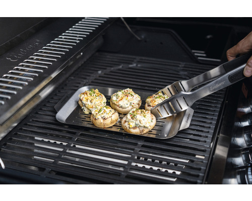 Gefüllte Champignons auf einer Grillplatte mit Grillzange auf einem Grill.