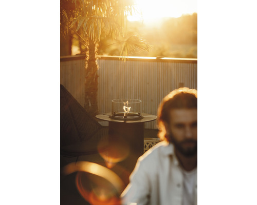 Tischkamin auf einer Terrasse mit Mann und Palmen im Hintergrund