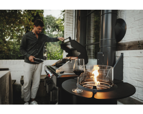 Szene mit einem Mann, der im Garten grillt, einem Glas Rotwein und einer Feuerstelle