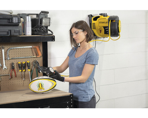 Frau pumpt Rugbyball mit Reifenfüller und Kompressor in Werkstatt auf