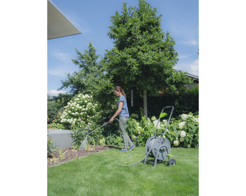 Frau bewässert Pflanzen mit einem Gartenschlauch auf einer Schlauchtrommel im Garten.
