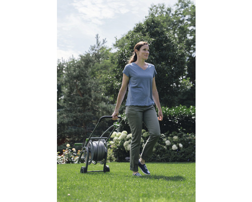 Frau zieht einen Schlauchwagen durch einen Garten