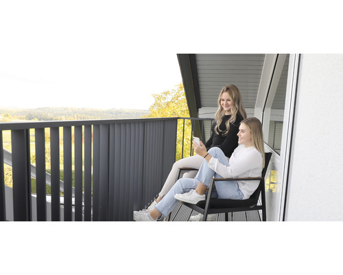 Zwei junge Frauen sitzen auf einem Balkon mit Geländer und genießen die Aussicht.