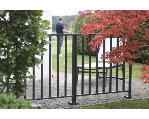 Zaun aus Metall im Außenbereich mit Gartenmöbeln und Laubbaum