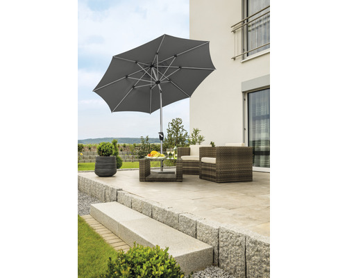 Szene mit einem Gartenschirm, Terrassenmöbeln und Pflanzen auf einer Steinterrasse.