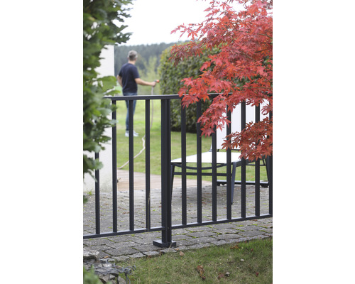 Gartenszene mit Zaun, rotem Ahorn und Person beim Bewässern des Gartens