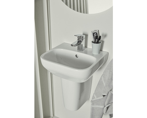Weißes Waschbecken mit Armatur, Zahnbürste und Zahnpasta im Badezimmer.