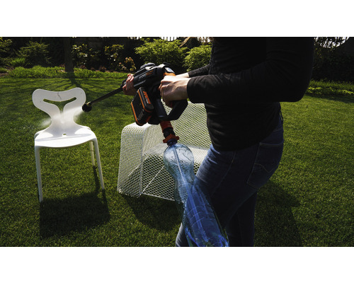 Eine Person benutzt einen Akku-Hochdruckreiniger, um einen Kunststoffstuhl im Garten zu reinigen. Eine Wasserflasche ist an den Hochdruckreiniger angeschlossen.