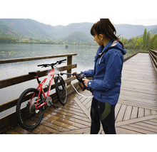 Eine Frau reinigt ein Fahrrad mit einem Hochdruckreiniger auf einem Holzsteg an einem See.