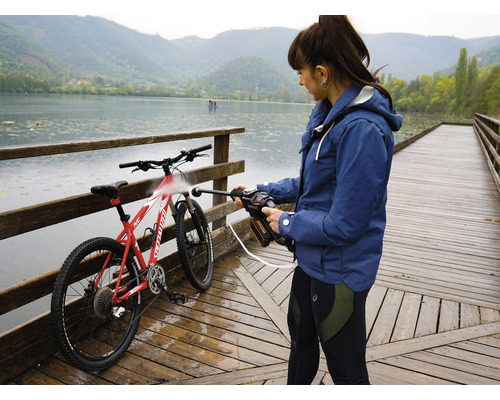 Eine Frau reinigt ein Fahrrad mit einem Hochdruckreiniger auf einem Holzsteg an einem See.