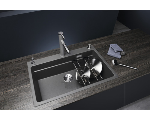 Spüle mit Armatur, Spülmittelspender, Abtropfgestell, Spültuch und Spülbürste auf einer dunklen Arbeitsplatte