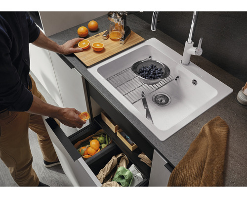 Küchenszene mit Spüle, Armatur, Abfallbehälter und Person, die eine Orange in den Abfall wirft.