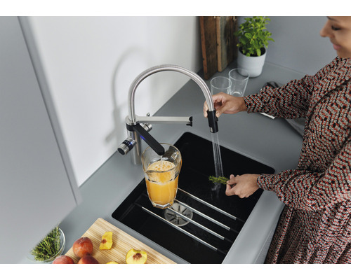 Frau wäscht Kräuter unter einem Wasserhahn in einer modernen Küche.