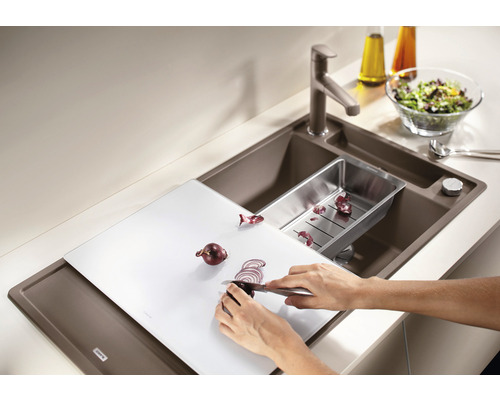 Küchenspüle mit Schneidebrett, Abtropfschale, Armatur und Person, die eine Zwiebel schneidet
