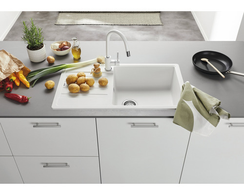 Küchenspüle mit Armatur, umgeben von Gemüse und Küchenutensilien.