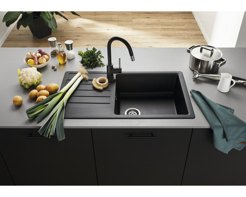 Schwarzes Spülbecken aus Granit mit Abtropffläche und Armatur auf einer Küchentheke mit Gemüse