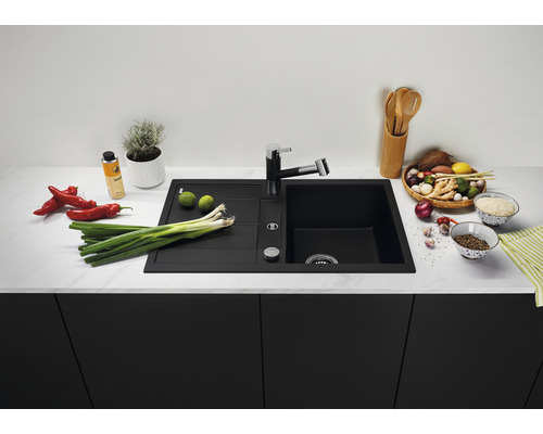 Schwarze Küchenspüle mit Abtropffläche und Armatur umgeben von Lebensmitteln auf einer Küchentheke.