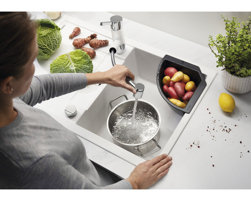 Frau befüllt Topf mit Wasser in einer Spüle mit Gemüse