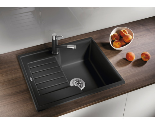 Schwarzes Spülbecken aus Verbundwerkstoff mit Abtropffläche und Armatur auf einer Arbeitsplatte mit Pfirsichen.
