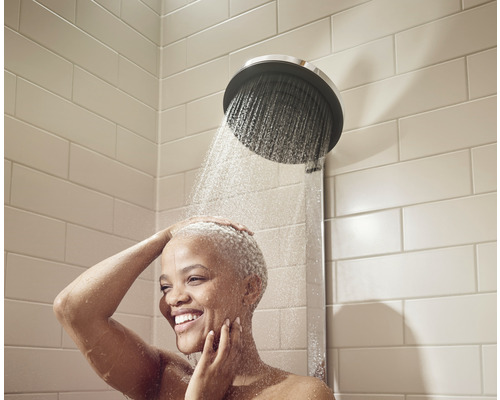 Frau unter einer Dusche mit Duschkopf und Fliesenwand